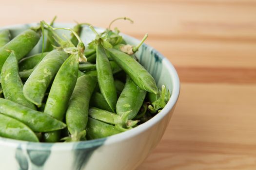 Green peas into a bowl. green peas in pods freshly picked on wood. Some green peas. Fresh green peas. green pods with peas as background.