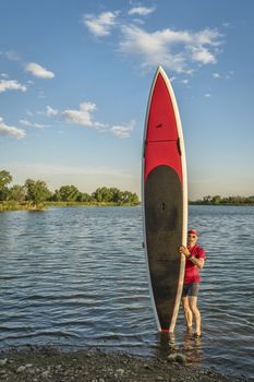 male paddler with his long stand up paddleboard on a lake shore