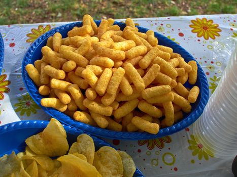 Crunchy cheese snacks puffs doodles in a blue bowl in a birthday garden party