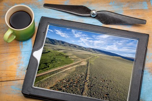 reviewing aerial picture on a digital tablet with a cup of coffee - foothills of Medicine Bow Mountains with a dirt road and cattle, North park, Colorado