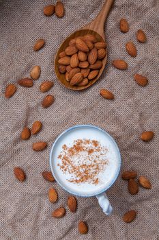 Homemade almond milk in Cup with whole almonds in wooden spoon on hemp sack background .