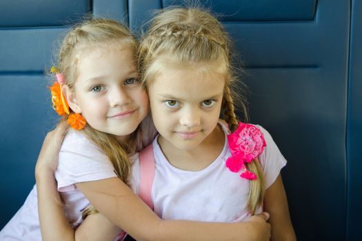 Two girls hugging look in the frame, sitting in an electric train, close-up