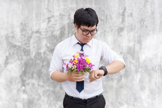 Waiting for his girlfriend. Close up of handsome young man holding bouquet of flowers stand in front of the concrete wall .