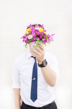 Waiting for his girlfriend. Close up of handsome young man holding bouquet of flowers stand in front of the concrete wall .