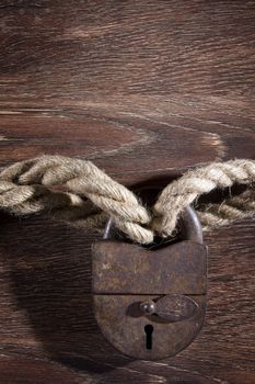 Old rusty lock with rope on wood background.