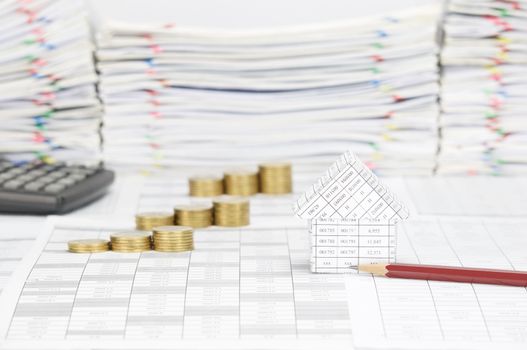 House and brown pencil on finance account have blur step pile of gold coins with calculator and overload of paperwork with colorful paperclip as background.