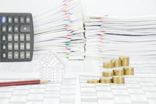 House and brown pencil with step pile of gold coins on finance account have blur  calculator place vertical and overload of paperwork with colorful paperclip as background.