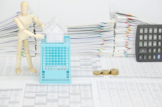 Wooden dummy holding house on blue basket with finance account have blur step pile of gold coins and calculator place vertical with pile overload document of report with colorful paperclip as background.