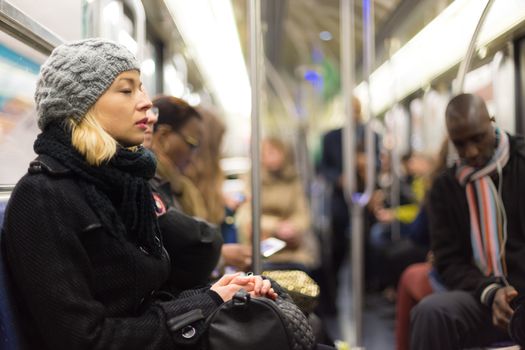 Beautiful blonde caucasian lady, wearing winter coat, napping while traveling by metro in rush hour. Public transport.