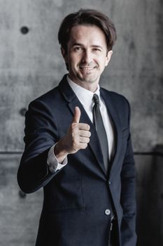 Portrait of businessman in suit showing thumb up sign over concrete wall background
