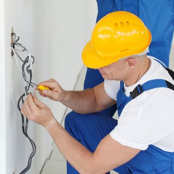 Two builders in helmets working with electricity indoors