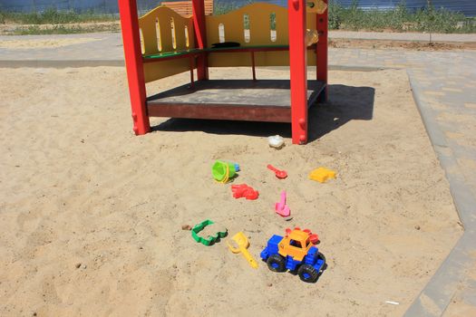 Children's sandbox with yellow sand and bright plastic toys