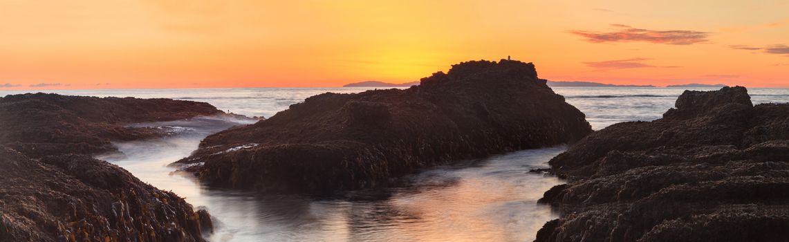 Long exposure of sunset over rocks, giving a mist like effect over ocean in Laguna Beach, California, United States