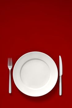 A white dish fork and knife on a red dinner table