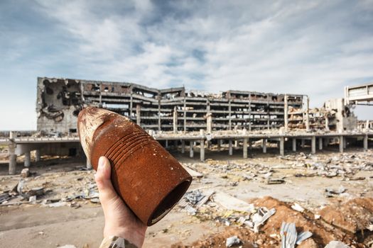 Unexploded 120 mm artillery shell in hand with destroyed Donetsk airport ruins on background