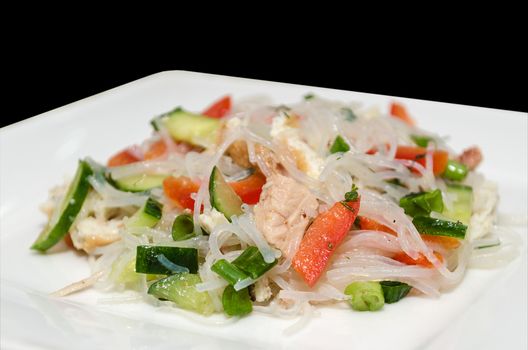 Salad funchoza with meat and vegetables on a white plate and isolated on a black background.