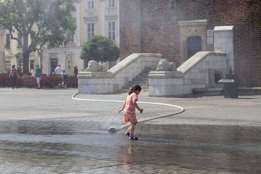 KRAKOW, POLAND - June 26, 2016 : Small girl using  water curtain on main Market Square in sunny day in summer.Curtains  are placed by  firefighters in the big heat in several places in the city