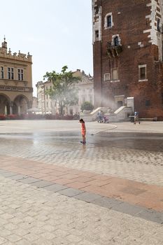 KRAKOW, POLAND - June 26, 2016 : Small girl using  water curtain on main Market Square in sunny day in summer.Curtains  are placed by  firefighters in the big heat in several places in the city