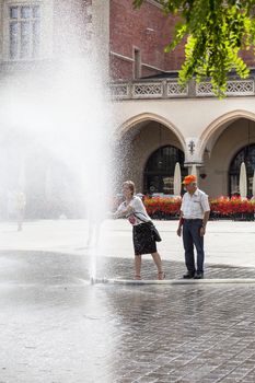 KRAKOW, POLAND - June 26, 2016 : People using  water curtain on main Market Square in sunny hot day in summer.Curtains  are placed by  firefighters in the big heat in several places in the city