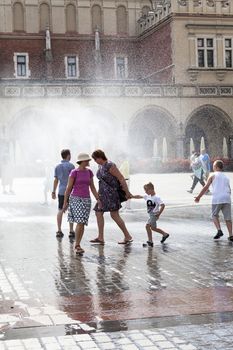 KRAKOW, POLAND - June 26, 2016 : People using  water curtain on main Market Square in sunny hot day in summer.Curtains  are placed by  firefighters in the big heat in several places in the city