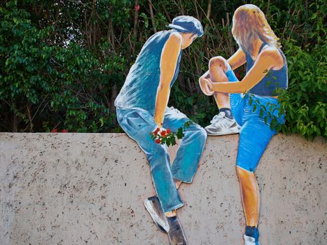 Beautiful creative street art graffiti of a young woman and man sitting on a fence