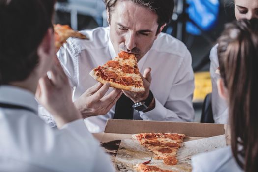 Business team eating pizza in office sitting around the table