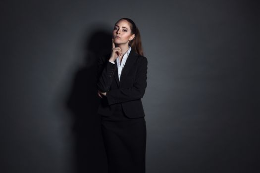 Portrait of young businesswoman in black suit on dark background