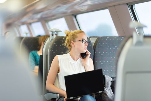 Businesswoman talking on cellphone and working on laptop while traveling by train. Business travel concept.