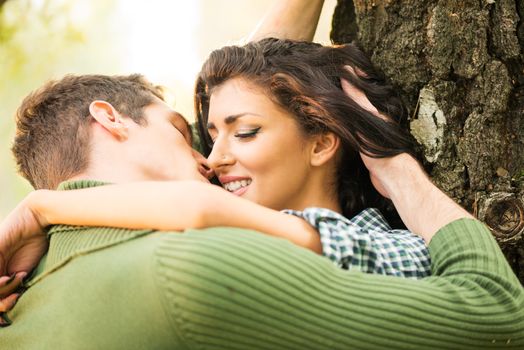 Close-up boy and girl kissing in a passionate embrace leaning against the tree.