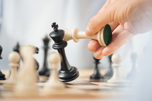 Close-up of human hand holding a white chess king over the chessboard, while crashes black chess king.