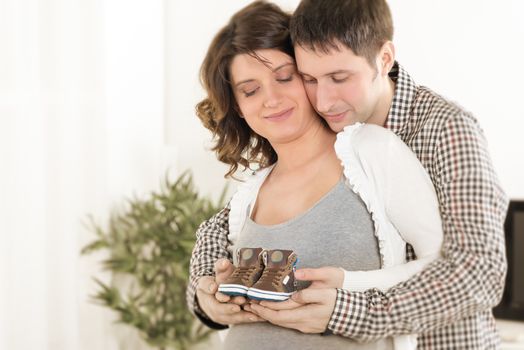 Portrait of a beautiful young couple holding baby shoes to the woman's pregnant belly.