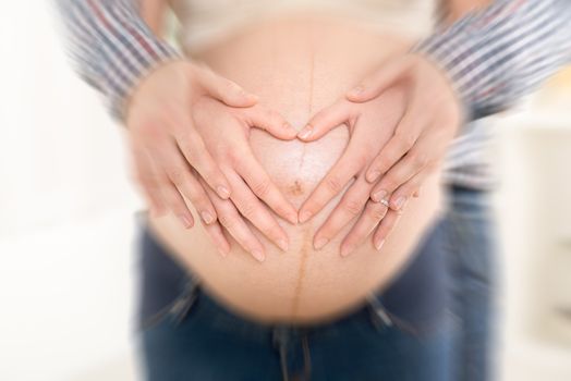 Male and female hands making a heart shape on the woman's pregnant belly.