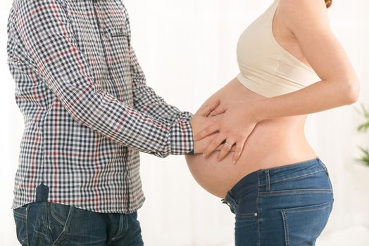 Male and female hands cuddling the woman's pregnant belly. 