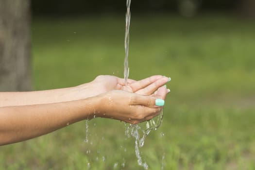 A stream of fresh clean water flowing to the hands of a girl with beautiful manicure