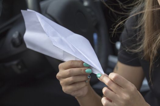 Paper plane in the hands of a girl with beautiful manicure sitting in the car.