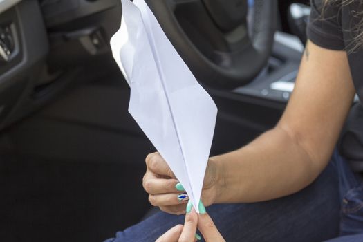 Paper plane in the hands of a girl with beautiful manicure sitting in the car.