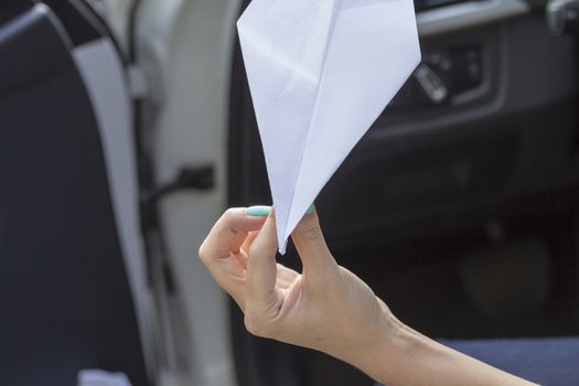 Paper plane in the hands of a girl with beautiful manicure sitting in the car.