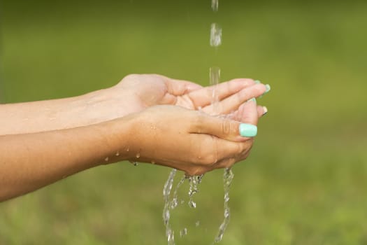 A stream of fresh clean water flowing to the hands of a girl with beautiful manicure