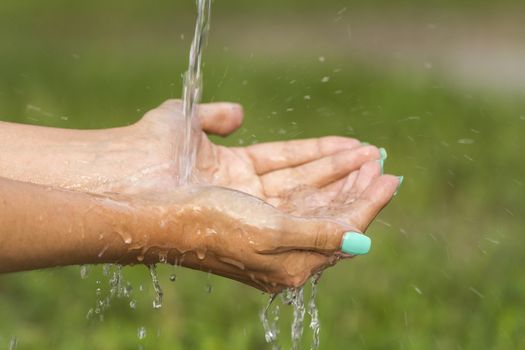 A stream of fresh clean water flowing to the hands of a girl with beautiful manicure