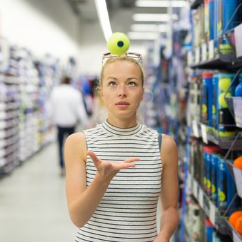 Beautiful caucasian woman shopping sports equipment in sportswear store. Lady throwing tennis ball in the air.