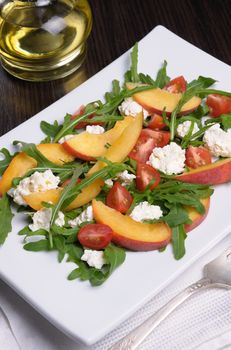 Salad with slices of peach, cherry tomatoes, arugula, feta