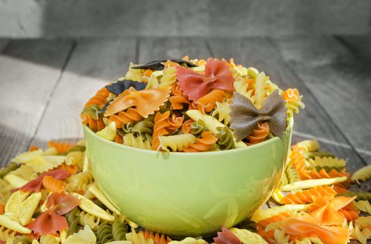 A variety of pasta, in a bowl and scattered around on the old boards.