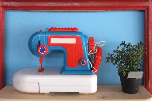 Toy and vintage sewing machine on blue background with pot of plant