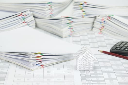 House and pile paperwork of report with colorful paperclip on finance account have blur pencil and calculator with pile overload document as background.