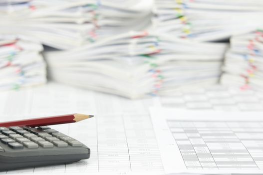 Pencil place on calculator with finance account have blur pile paperwork of report with colorful paperclip as background.