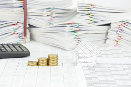 House and step pile of gold coins on finance account have blur pencil place vertical and calculator with pile paperwork of report with colorful paperclip as background.