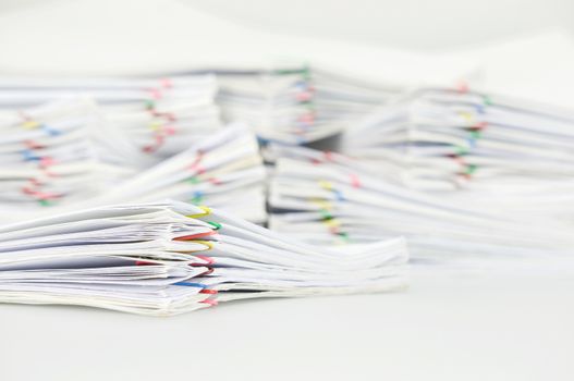 Pile paperwork of report with colorful paperclip on white table have blur pile overload document as background.