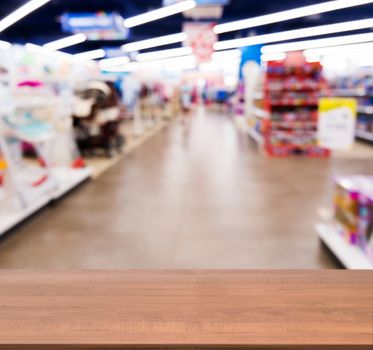 Wooden board empty table in front of blurred background. Perspective dark wood table over blur in kids toy store. Mock up for display or montage your product.