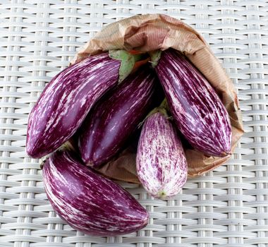 Heap of Fresh Raw Striped Eggplants into Paper Bag closeup on Wicker background