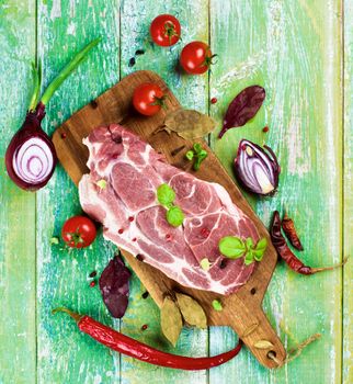 Perfect Raw Pork Neck with Spices, Ripe Tomatoes, Halves of Red Onion, Herbs and Fresh Basil Leaves closeup on Wooden Cutting Board. Top View